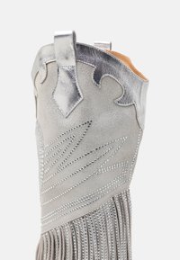 Stříbrná kožená bota s dekorativním třásněm, strukturální šedou semišovou částí a akcenty z rhinestone, s vlnitým vrškem a poutky na stažení.