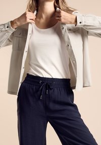 Ljusgrå skjorta med knappar över en vit linne, kombinerad med marinblå byxor med dragsko, mjuk textur och avslappnad passform.