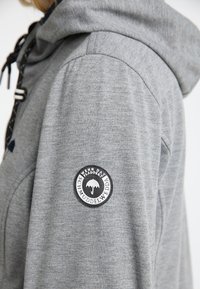 Hoodie gris avec une texture douce, cordons de serrage réglables et un badge circulaire sur la manche avec un graphique de parapluie noir.