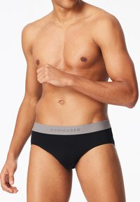 Culotte noire en coton avec une ceinture grise arborant le logo "Schiesser". Le design est simple et ajusté, mettant en avant un style classique.