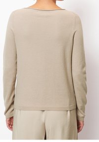 Beige Pullover mit langen Ärmeln und runder Ausschnitt; weiches, strukturiertes Material und gerippter Saum. Getragen mit hellen Hosen.