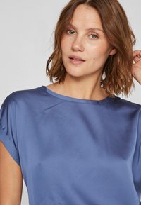 Sateng blå topp med løs passform, korte ermer og rund hals, med en jevn tekstur og subtil glans.