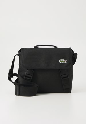 Bolsa mensajera negra con un tejido texturizado. Cuenta con una tapa plegable, una correa ajustable y un pequeño logotipo de cocodrilo bordado.