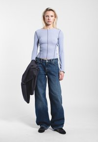 Light purple long-sleeve top with ribbed texture, featuring contrasting seams; paired with high-waisted, dark blue wide-leg jeans.