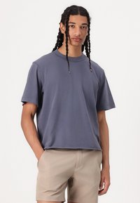T-shirt gris à manches courtes en tissu doux, avec un col rond et une coupe décontractée, associé à un short beige clair.