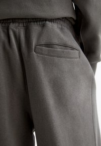 Grå sweatpants med elastisk midjeband och en böjd sidoficka. Mjuk, texturerad tyg. Nära bild som visar fickdetalj.