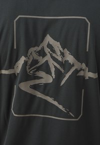 Camiseta de tela gris oscura que presenta un gran gráfico de montaña gris clara con un diseño de carretera serpenteante, enmarcado en un contorno rectangular.