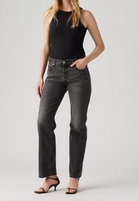 Svarta denimjeans med rak ben-design, blekt utseende, fem fickor och knappstängning. Matchade med en svart linne och sandaler.