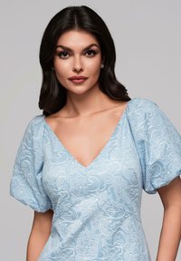 Robe bleu clair avec un design en dentelle florale texturée, manches courtes bouffantes et décolleté en V, soulignant son apparence délicate et complexe.