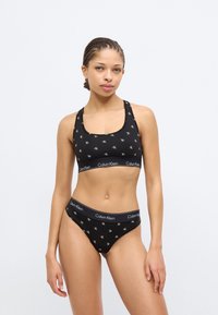Μαύρο βαμβακερό αθλητικό μπουστάκι και αντίστοιχο κάτω μέρος μπικίνι με λευκή εκτύπωση λογότυπου CK, με φαρδιά ελαστική μέση. Λείο, εφαρμοστό σχέδιο.