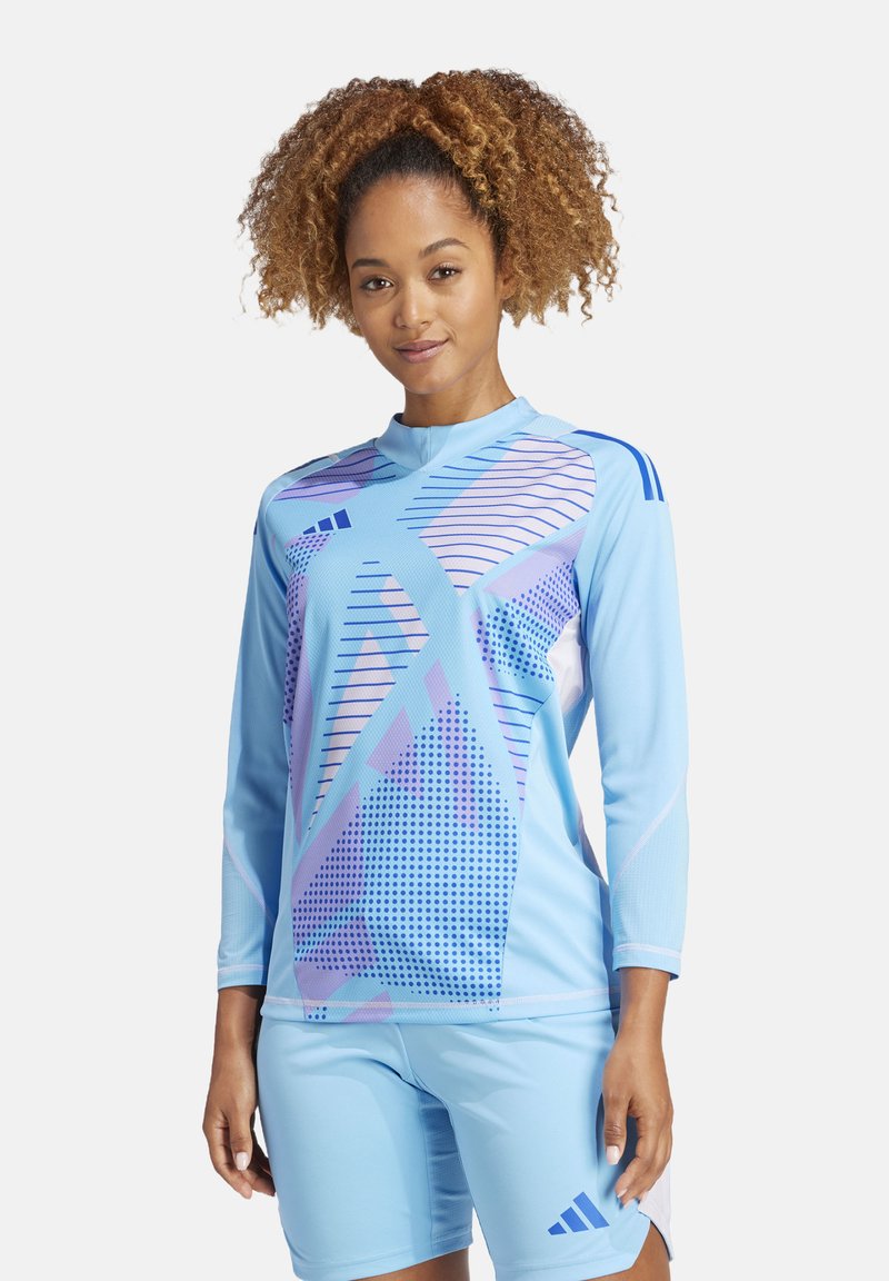 Lichtblauwe sportoutfit met een langmouwen top met geometrische patronen in paars en blauw, en shorts met merkaccenten.