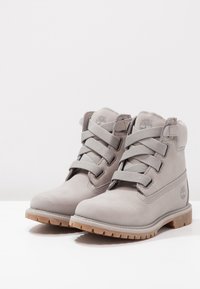 Gray leather ankle boots with six eyelets, textured fabric laces, and a rubber sole with a traction pattern. Timberland logo featured.