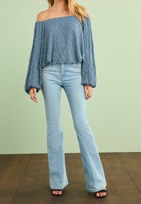 Lys blå off-shoulder tekstureret sweater med lange ærmer, parret med lys blå flared jeans og sorte slidesandaler.