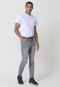 Pantalones jogger de denim gris con cinturilla y puños elásticos, combinados con una camiseta blanca sencilla y zapatillas negras.
