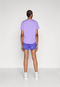 Μωβ πουκάμισο με κοντό μανίκι και στρογγυλεμένο τελείωμα, συνδυασμένο με μπλε σορτς που έχουν λευκές λεπτομέρειες με κουμπιά. Και τα δύο είναι κατασκευασμένα από ελαφρύ, διαπνέον υλικό.