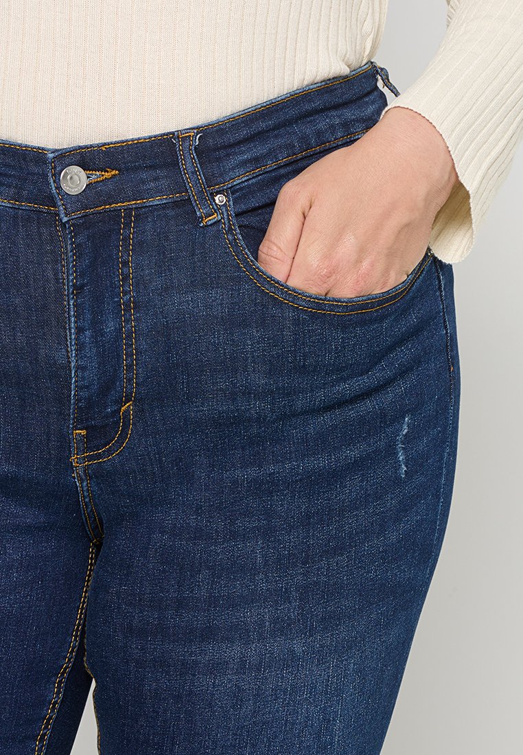Dunkelblaue Denim-Jeans mit einem Fünf-Taschen-Design, sichtbaren Nähten in Orange und einer leichten Used-Optik am Oberschenkel.