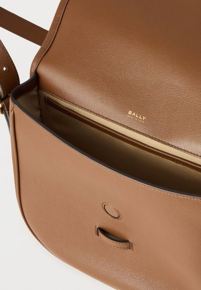 Καφέ δερμάτινη τσάντα χιαστί με λεία υφή, που διαθέτει χρυσό λογότυπο, επάνω καπάκι κλεισίματος και εσωτερική τσέπη για οργάνωση.