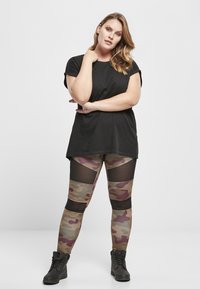 Black t-shirt, camouflage leggings featuring mesh panels, and black ankle boots. The leggings display shades of green, brown, and burgundy.