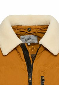 Tan zip-up jacket met een crèmekleurige schapenvacht kraag, voorste ritssluiting en een buitenzak. Heeft een merklabel en verzorgingsinstructies aan de binnenkant.