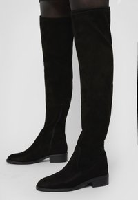 Svarta mocka över knästövlar med klack och sidodragkedja. Slät yta och åtsittande design, med rund tåform.