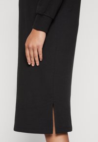 Schwarzes Baumwollkleid mit langen Ärmeln, das einen Seitenschlitz am Saum und gerippte Bündchen aufweist und ein einfaches und elegantes Design betont.