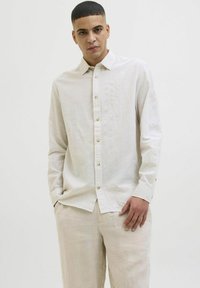 Camisa de botones a rayas claras en beige y colores pastel. Presenta un cuello clásico y botones dorados, fabricada con un tejido suave y texturizado.