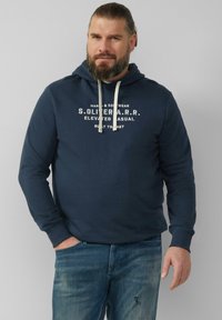 Granatowa bluza z kapturem z grafiką na przodzie w białym kolorze. Posiada kaptur ze sznurkiem oraz ściągacze przy rękawach. Zestawiona z wyblakłymi niebieskimi dżinsami.