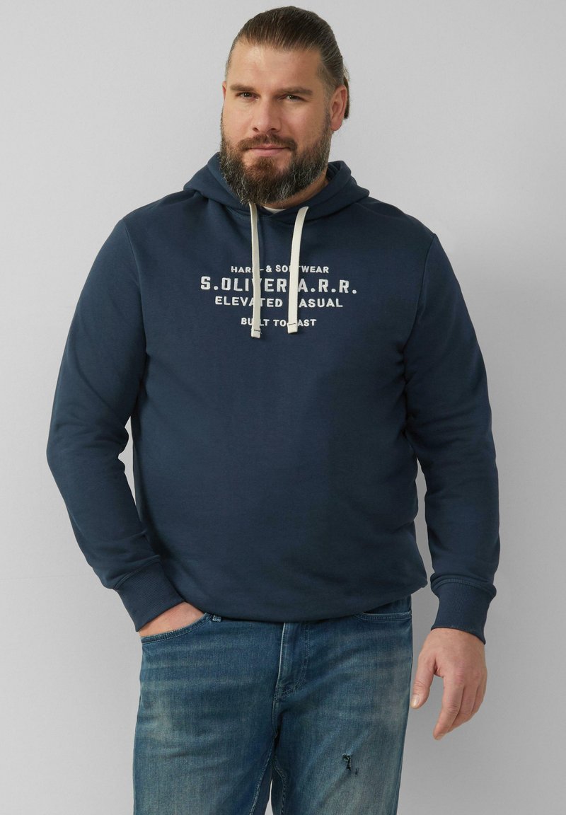 Granatowa bluza z kapturem z grafiką na przodzie w białym kolorze. Posiada kaptur ze sznurkiem oraz ściągacze przy rękawach. Zestawiona z wyblakłymi niebieskimi dżinsami.