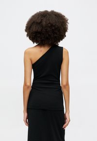 Musthave mustraga top, mille venitanud kangast. Omab tihedat disaini, kihilise ääre ja nähtava tätoveeringu õlal.