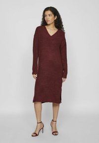 Robe tricotée bordeaux avec un décolleté en V, des manches longues et des fentes sur les côtés. Le tissu semble doux avec une finition texturée.