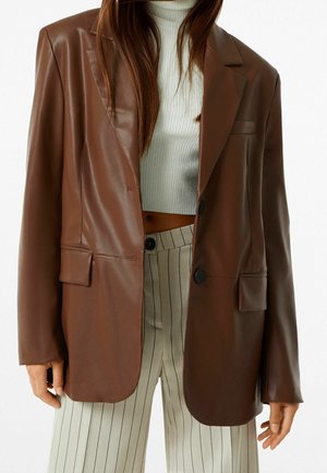 Bruine faux leren blazer met een gestructureerd ontwerp, twee voorzakken, een knoopsluiting met één knop en geknipte revers, gecombineerd met gestreepte broeken.