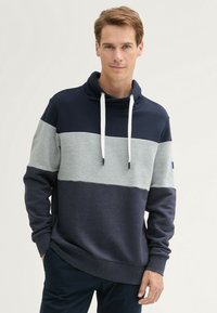Sudadera a rayas en azul marino y gris con cuello vuelto, cierre de cordón y mangas largas. Textura suave y corte relajado.