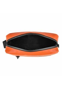 Oranžová kožená taška s hladkým povrchem, vybavená horním zipem a černým interiérem. Design je obdélníkový s zaoblenými hranami.