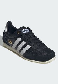 Black athletic shoe with white three-stripe design, perforated leather upper, suede accents, rubber sole, and "adidas Japan" branding.