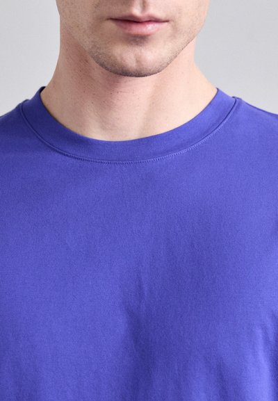 T-shirt en coton violet avec un col rond. Le tissu semble doux, avec une texture lisse et sans motifs ni accents visibles.