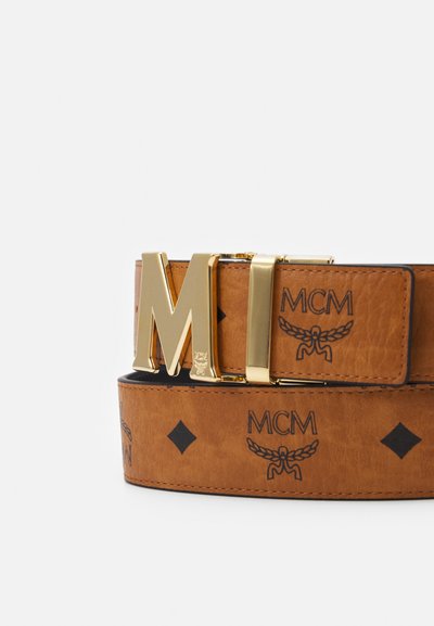Brun läderbälte med en gul metallspänne i form av "M", präglad MCM-logotyp och diamantmönster. Slät textur med kontrasterande svarta accenter.