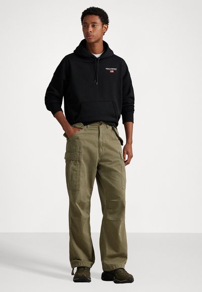 Hanorac negru cu buzunar frontal, având logo-ul "POLO SPORT". Pantaloni cargo verde măsliniu, cu buzunare laterale și glezne strânse. Încălțăminte neagră.