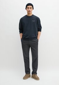 Marineblaues Langarmshirt mit Rundhalsausschnitt, graue Hose und sandfarbene Wildlederschuhe. Einfaches Design, maßgeschneiderte Passform und weiche Textur.