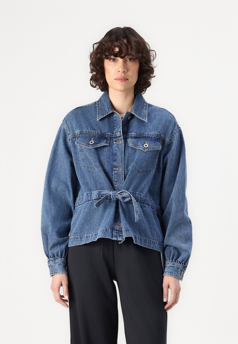 Veste en denim avec une taille ceinturée, deux poches poitrine, fermeture à boutons sur le devant et manches longues. Couleur bleu clair à moyen avec une coupe décontractée.