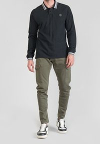 Czarna, długorękawowa koszulka polo z białym paskowanym kołnierzykiem, zestawiona z oliwkowymi spodniami cargo z wieloma kieszeniami oraz czarnymi sneakersami.