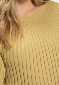 Gelber gerippter Strickpullover mit rundem Halsausschnitt. Der Stoff hat eine weiche Textur mit vertikalen Streifen und dezenten Nähten.