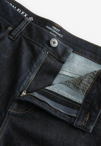 Pantalones vaqueros de mezclilla oscura con un ajuste slim, que cuentan con un cierre de botón metálico y cremallera, costuras en contraste y un forro de bolsillo interior estampado.