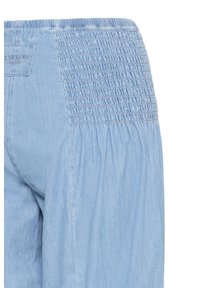 Šviesiai mėlyni džinsai su elastingu rauktu juosmeniu ir susmulkinta medžiaga šone, matoma galinė kišenė su siuvinėtu prekės ženklo etikete.