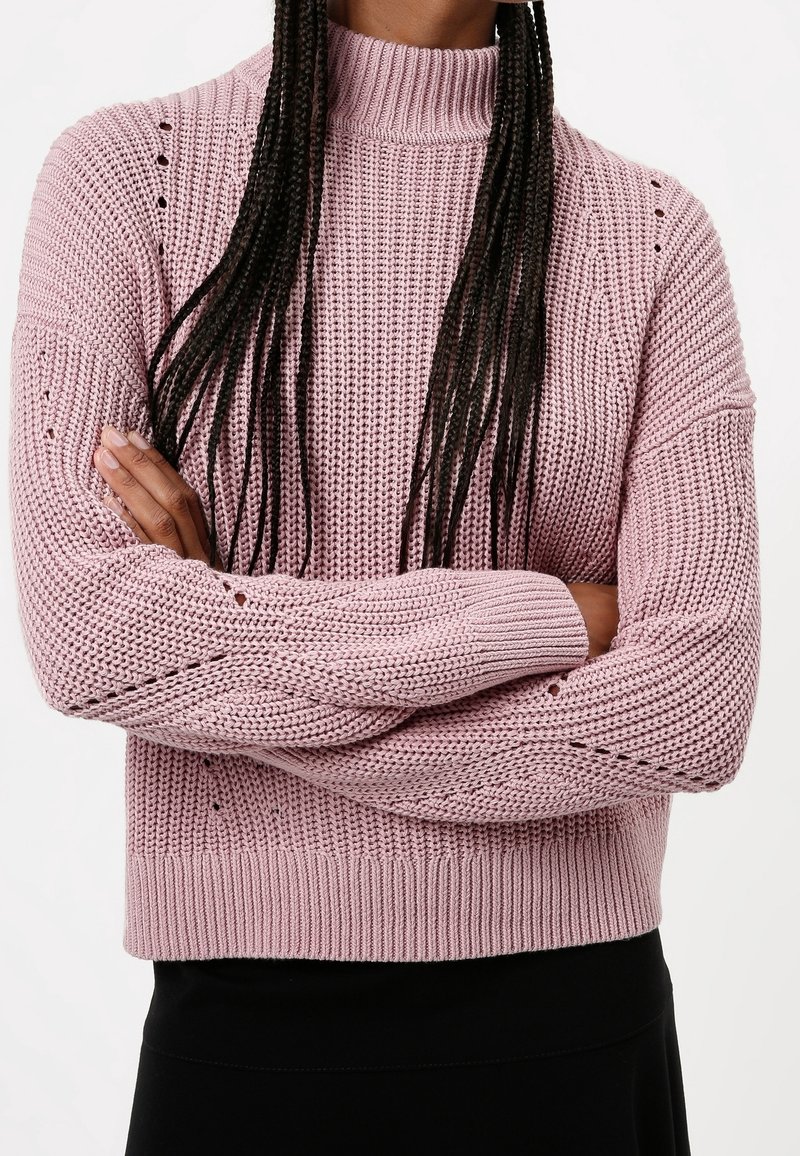 Krótki, różowy sweter z krótkim rękawem, z wysokim kołnierzem, z otwartymi detalami na ramionach i luźnym krojem.