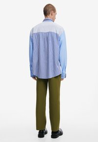 Hellblau und weiß gestreiftes, oversized Hemd mit langen Ärmeln, kombiniert mit grünen, weiten Hosen und schwarzen Schuhen. Die Textur wirkt glatt.