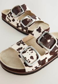 Bruna och vita sandaler med ko-mönster, med två justerbara silverfärgad spännen, som har en mjuk interiör och en texturerad sula för bra grepp.