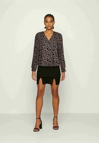 Blusa de manga longa em roxo escuro com padrão floral preto, combinada com uma saia preta justa com abertura à frente, e saltos pretos.