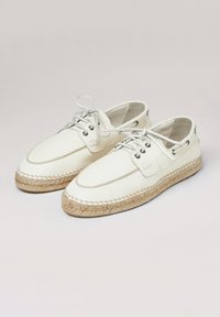 Zapatos de cuero blanco con suela de yute trenzado. Presentan un diseño con cordones, ojales de metal y detalles de costura a lo largo del borde de la suela.