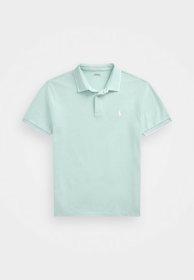 Camisa polo azul clara feita de algodão texturizado, com colarinho clássico, mangas curtas e um pequeno emblema bordado no peito.
