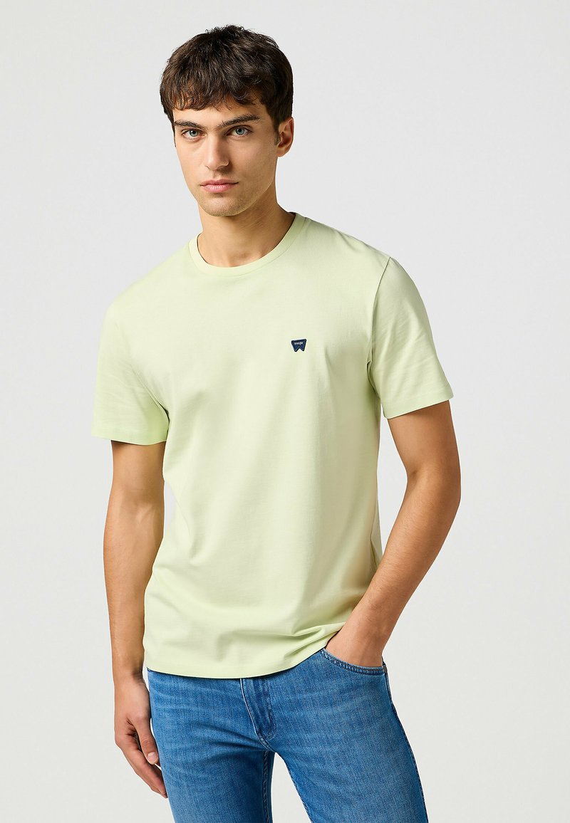 Ljusgul kortärmad t-shirt i mjukt tyg med en liten marinblå logotyp på vänster bröst och en klassisk rundad halsringning.